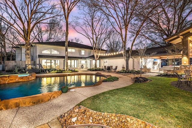 pool at dusk featuring fence, an outdoor pool, a yard, a patio area, and an in ground hot tub