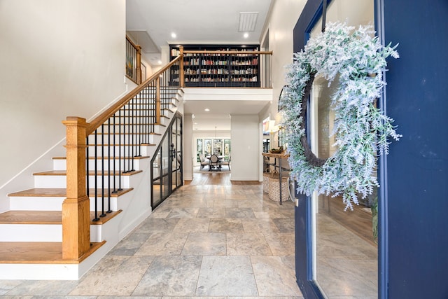 foyer entrance with stone tile flooring, stairway, baseboards, and a towering ceiling