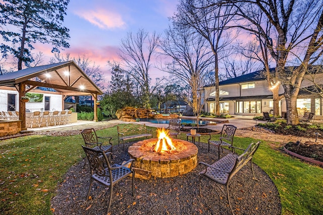 yard at dusk featuring a gazebo, an outdoor pool, a patio area, and an outdoor fire pit