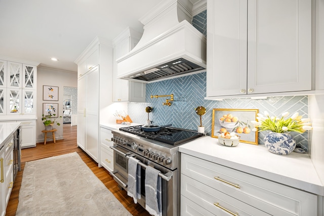 kitchen with range with two ovens, decorative backsplash, custom exhaust hood, white cabinets, and dark wood-style flooring