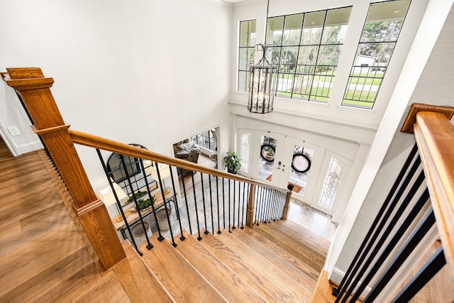 staircase with wood finished floors, baseboards, ornamental molding, a towering ceiling, and a chandelier