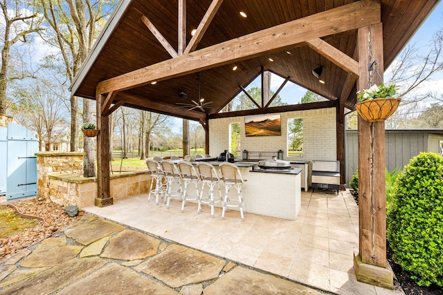 view of patio featuring a gazebo, outdoor wet bar, a ceiling fan, fence, and an outdoor kitchen