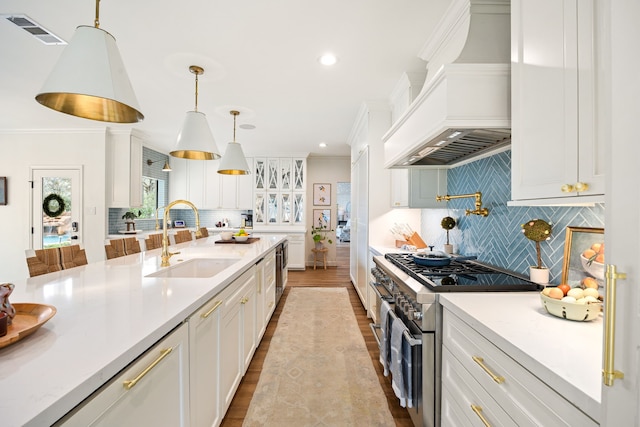 kitchen featuring visible vents, a sink, high end range, white cabinetry, and custom range hood
