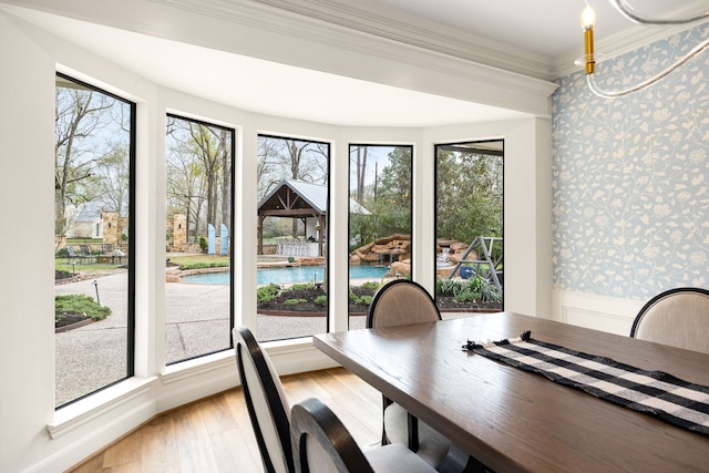 dining area featuring wainscoting, crown molding, wallpapered walls, and light wood-type flooring