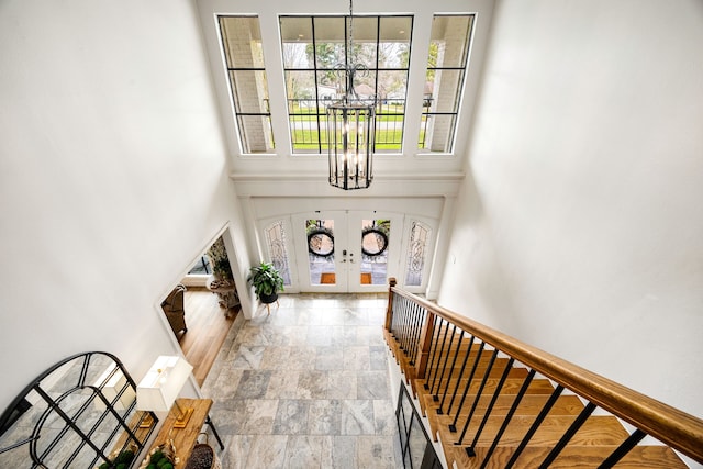 entryway featuring stairway, a chandelier, french doors, stone finish flooring, and a high ceiling