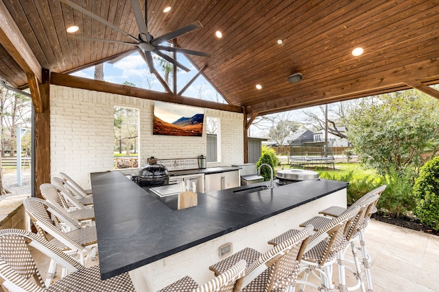 view of patio / terrace with a ceiling fan, a sink, a trampoline, outdoor wet bar, and exterior kitchen