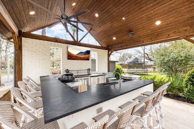view of patio featuring outdoor wet bar, a ceiling fan, exterior kitchen, and a sink