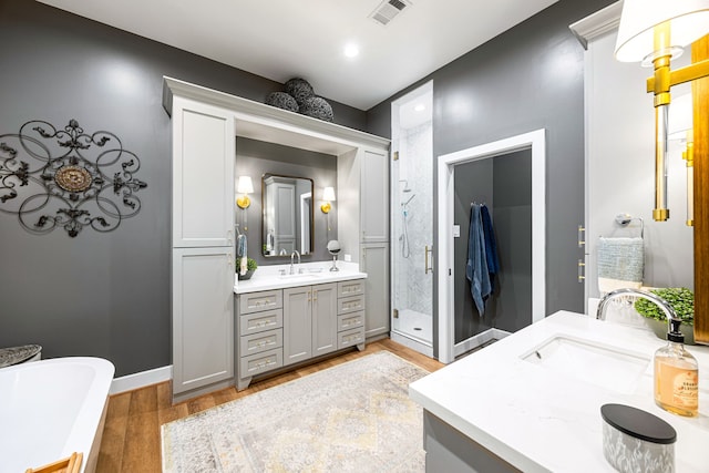 full bath featuring visible vents, a shower stall, two vanities, wood finished floors, and a sink