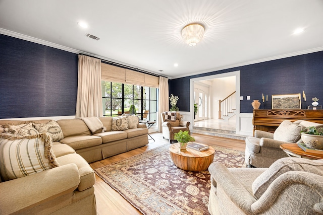 living room with visible vents, wallpapered walls, crown molding, stairway, and wainscoting