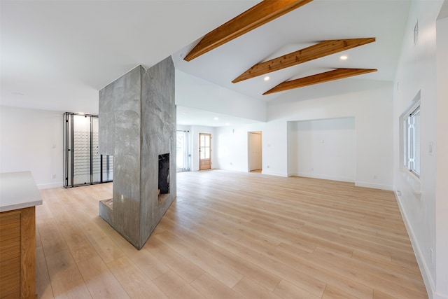 unfurnished living room featuring beam ceiling, high vaulted ceiling, light wood-style flooring, and a fireplace