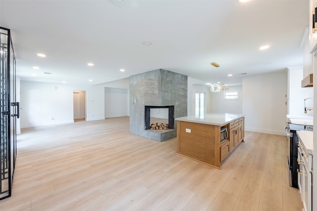 kitchen with open floor plan, light wood-type flooring, brown cabinets, a tile fireplace, and stainless steel appliances