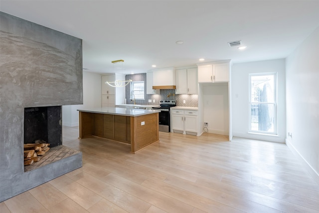 kitchen with stainless steel electric range oven, light wood-style floors, a fireplace with raised hearth, and white cabinets