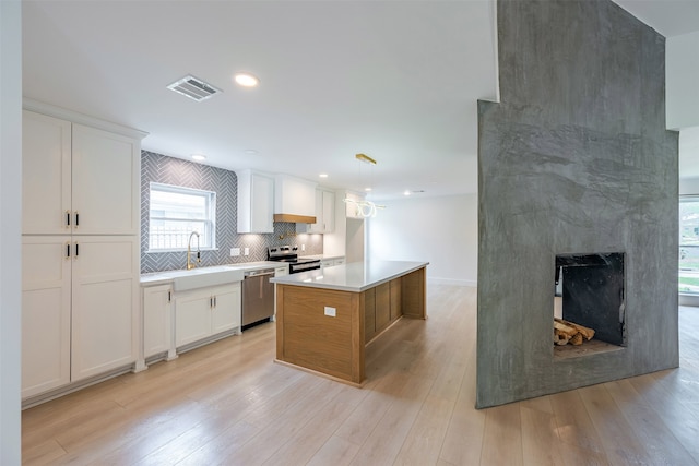 kitchen featuring visible vents, light wood finished floors, a sink, decorative backsplash, and stainless steel appliances