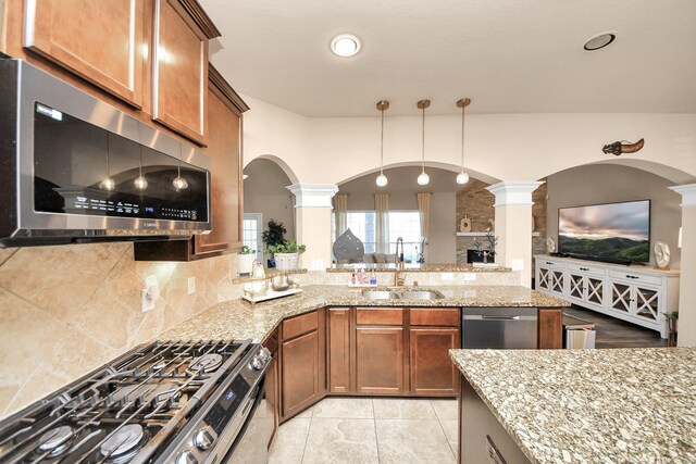 kitchen featuring brown cabinets, a sink, tasteful backsplash, appliances with stainless steel finishes, and decorative columns