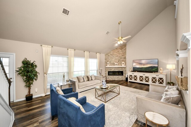 living room featuring a stone fireplace, dark wood-style flooring, visible vents, and a wealth of natural light