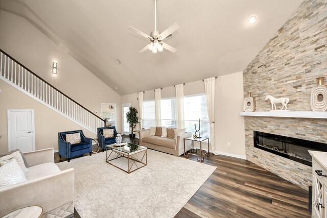 living area featuring high vaulted ceiling, a ceiling fan, dark wood-style floors, a stone fireplace, and stairs