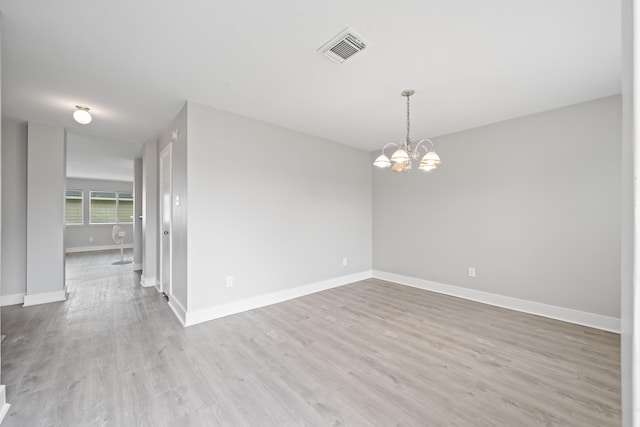 unfurnished room with an inviting chandelier, wood finished floors, visible vents, and baseboards