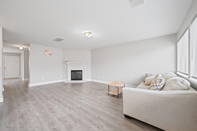 living area with visible vents, baseboards, light wood-style floors, and a glass covered fireplace