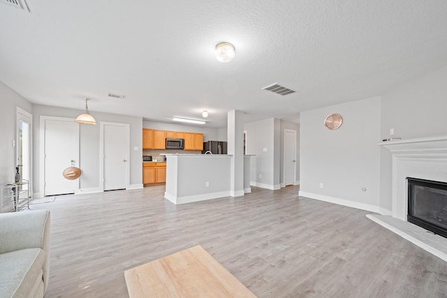 unfurnished living room with visible vents, baseboards, light wood-style floors, and a glass covered fireplace