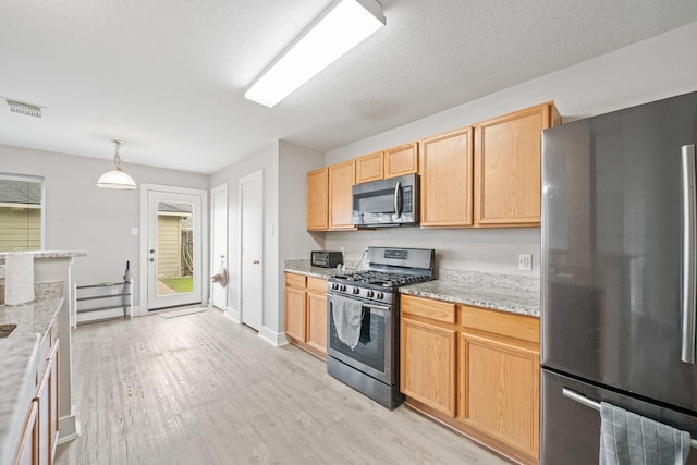 kitchen with visible vents, light brown cabinets, appliances with stainless steel finishes, light wood-style floors, and hanging light fixtures