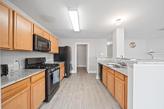 kitchen with light stone countertops, light wood finished floors, a sink, black appliances, and a textured ceiling