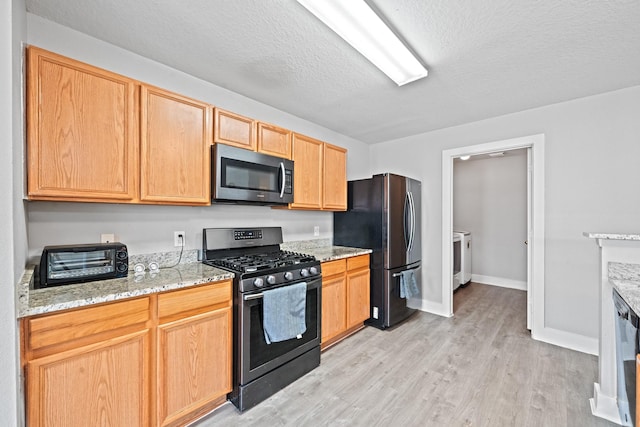 kitchen with a toaster, light stone counters, light wood-style flooring, stainless steel appliances, and a textured ceiling