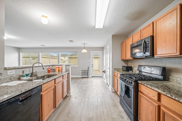 kitchen featuring dishwasher, stone counters, light wood-style flooring, stainless steel gas stove, and a sink