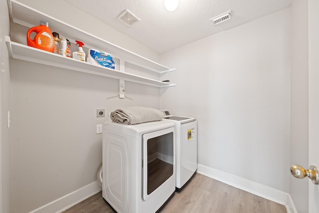 clothes washing area with laundry area, light wood-style flooring, visible vents, and washer and clothes dryer