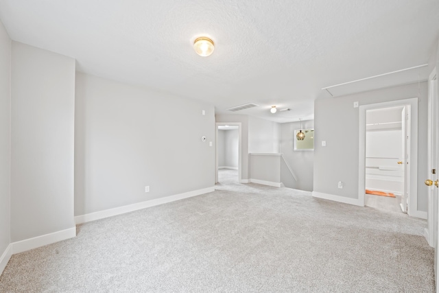 carpeted empty room with visible vents, a textured ceiling, attic access, and baseboards