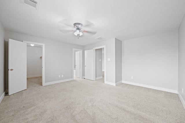 unfurnished bedroom featuring a walk in closet, baseboards, visible vents, and light carpet