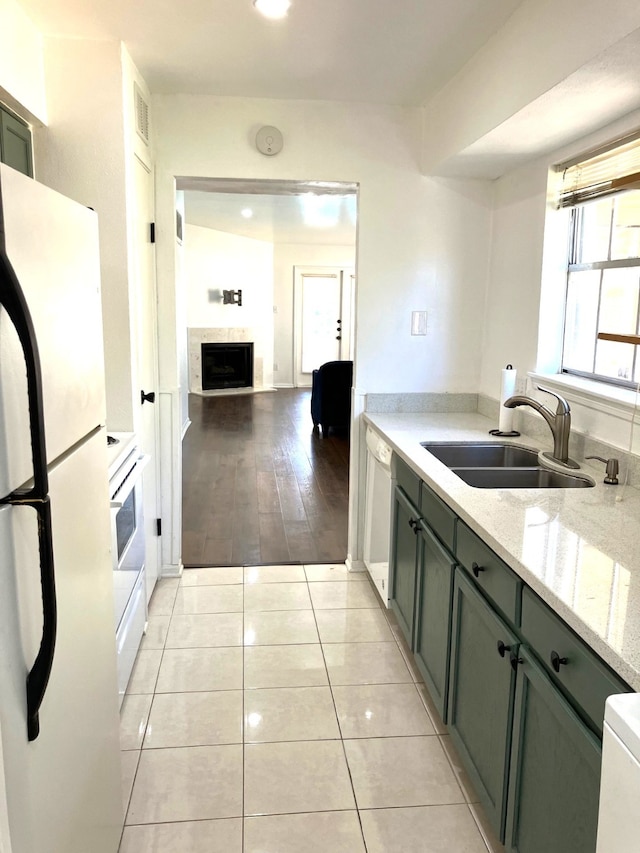 kitchen with a sink, white appliances, a fireplace, light tile patterned floors, and light stone countertops