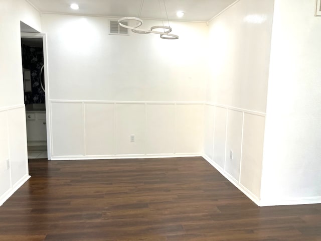 unfurnished room featuring a decorative wall, dark wood-style floors, visible vents, and ornamental molding