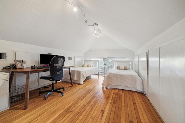 bedroom with light wood finished floors, a textured ceiling, and vaulted ceiling