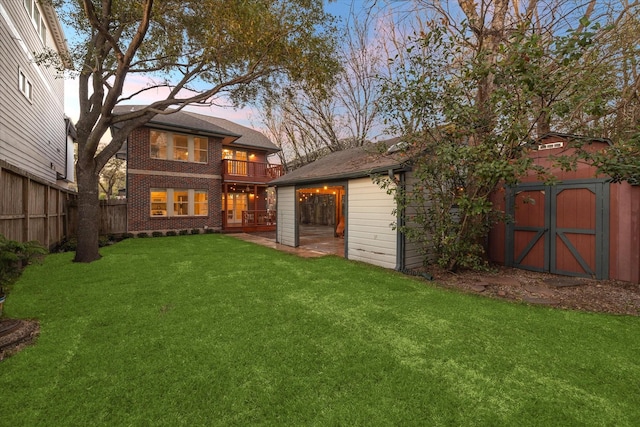 back of house at dusk featuring brick siding, fence, a storage shed, a yard, and an outbuilding