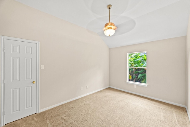 empty room featuring carpet flooring, baseboards, and vaulted ceiling