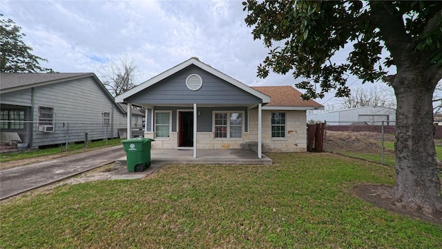 view of front facade with a front lawn, stone siding, a porch, fence, and roof with shingles