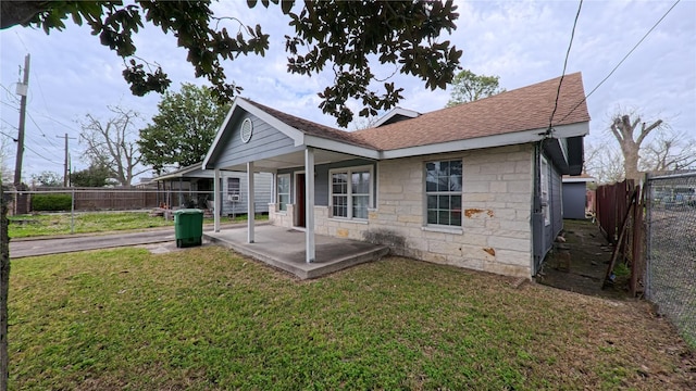 back of house with stone siding, a lawn, roof with shingles, and a fenced backyard