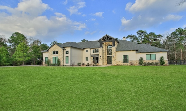 view of front of house featuring stucco siding, stone siding, a front yard, a shingled roof, and a chimney