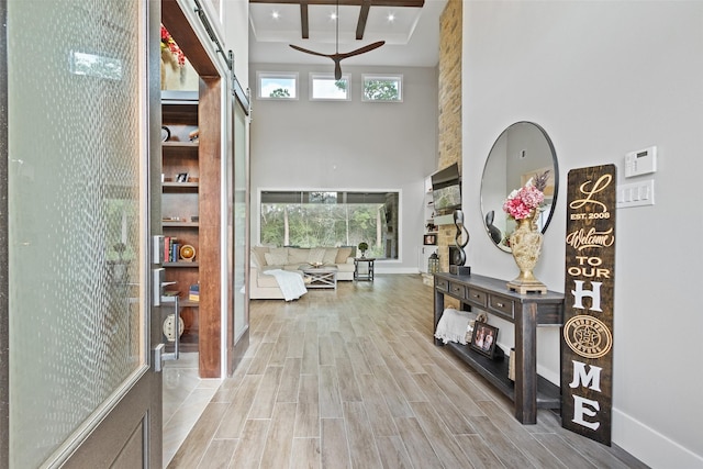 hallway with beam ceiling, baseboards, wood finish floors, and a towering ceiling