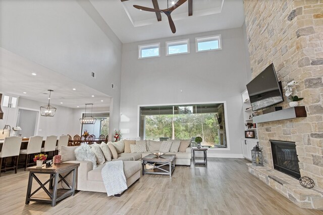 living area featuring light wood finished floors, a stone fireplace, ceiling fan with notable chandelier, and a wealth of natural light