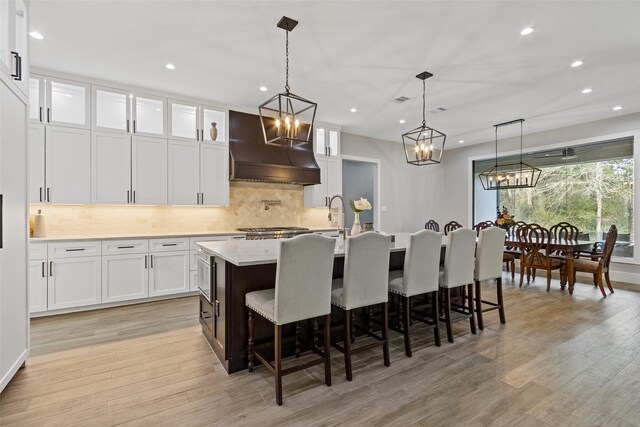 kitchen featuring light wood-type flooring, white cabinetry, decorative backsplash, and custom range hood