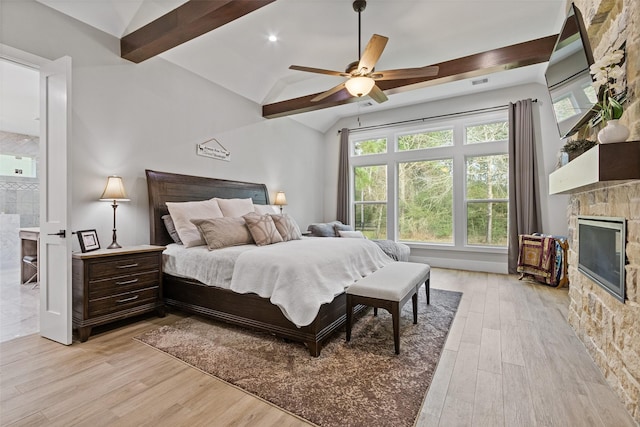 bedroom featuring a stone fireplace, vaulted ceiling with beams, a ceiling fan, and light wood finished floors