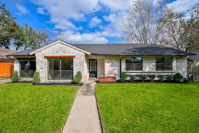 view of front of property featuring brick siding, a shingled roof, a front lawn, and fence