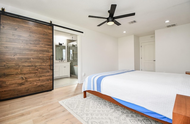 bedroom featuring ensuite bath, a barn door, light wood-style floors, and visible vents