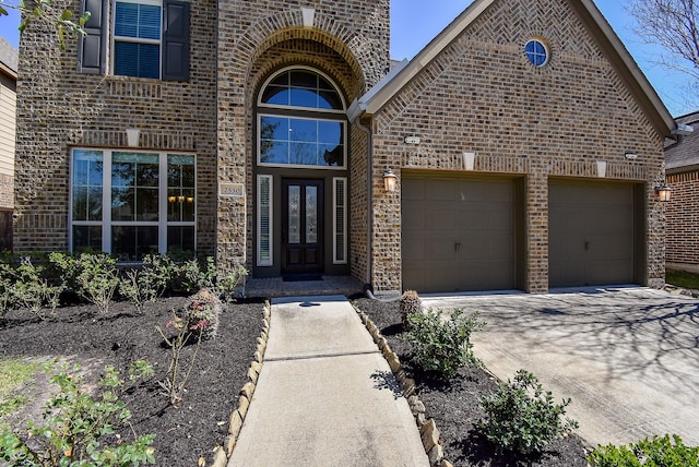 doorway to property featuring brick siding, driveway, and a garage