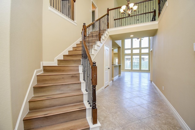 stairs with tile patterned floors, a high ceiling, a notable chandelier, and baseboards