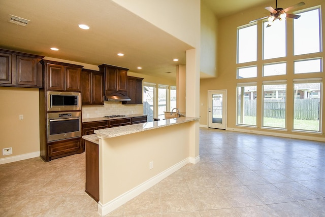 kitchen with light stone counters, visible vents, stainless steel appliances, under cabinet range hood, and backsplash