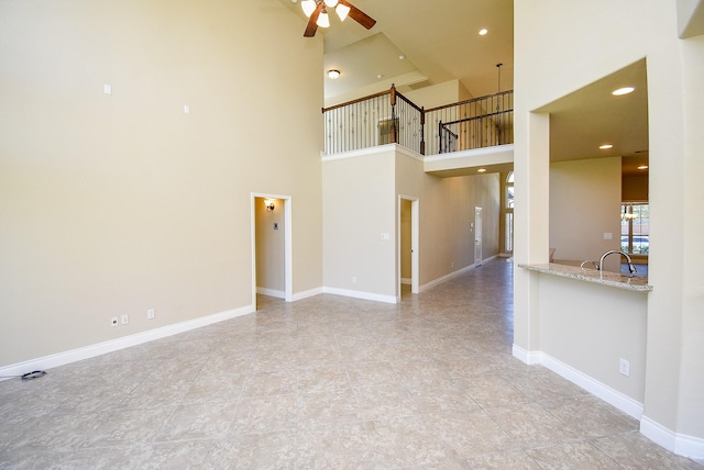 unfurnished living room with a high ceiling, recessed lighting, baseboards, and ceiling fan