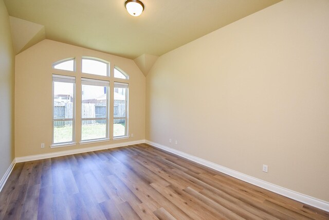 spare room featuring lofted ceiling, baseboards, and wood finished floors