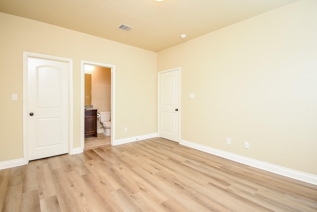 unfurnished bedroom featuring light wood-type flooring, baseboards, visible vents, and ensuite bathroom